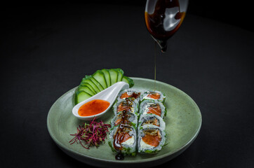 Fototapeta na wymiar Perfect sushi, traditional Japanese cuisine. Delicious uramaki with sweet and sour sauce on the decorated plate, black background.