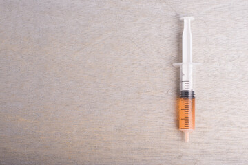 A syringe filled with orange color liquid isolated over grey wooden background