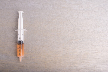 Fototapeta premium A syringe filled with orange color liquid isolated over grey wooden background
