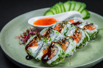Perfect sushi, traditional Japanese cuisine. Delicious uramaki with sweet and sour sauce on the decorated plate, black background.