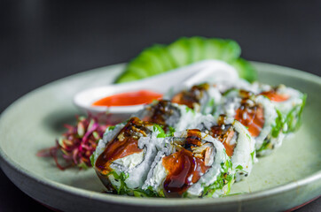 Perfect sushi, traditional Japanese cuisine. Delicious uramaki with sweet and sour sauce on the decorated plate, black background.