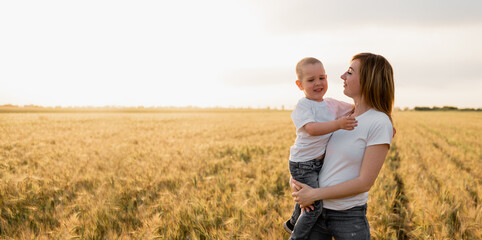 Young mother holding her baby in her arms in a wheat field. Holidays with children in the countryside. Beautiful sunset.