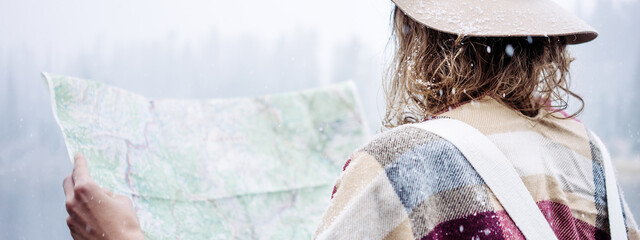 Travel woman reading map among amazing mountain wild, enjoy the nature landsape. Forest and lake, wearing hat and poncho, boho and wanderlust style. Wide screen, panoramic