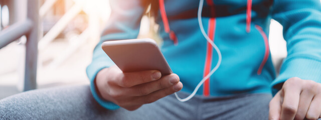 Woman runner using cell phone outdoors, on the city street. Wide screen, panoramic