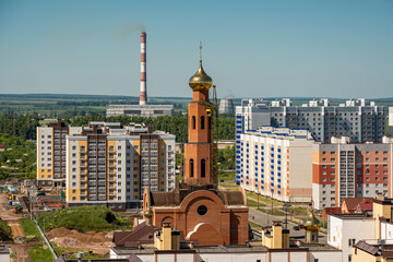 Landscape of the city outskirts with residential buildings, a Christian church under construction and a thermal power plant in the background