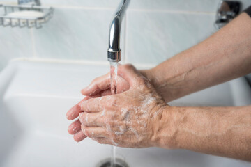 Fototapeta na wymiar Older male is washing his hand under faucet