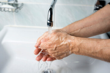 Older male is washing his hand under faucet