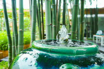 Closeup to little fountain from bamboo stick inside green vintage jar that decorated in the garden with sunlight effect.