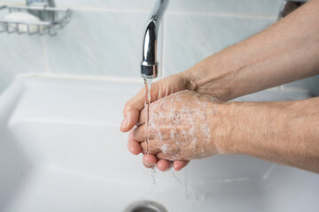 Older male is washing his hand under faucet