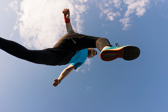 Low angle view of a sportsman who jump and run with blue sky in background