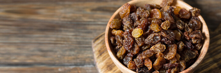 Raisins in a wooden bowl on the brown kitchen table. Raisins close-up. Banner with space for text