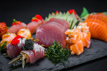 Sushi, traditional Japanese cuisine. Several delicious sushi on the decorated plate, black background. Group of sushi, Urakami, Nigori, Sushi jow, sashimi, tekamaki, etc ...