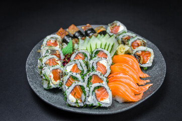 Sushi, traditional Japanese cuisine. Several delicious sushi on the decorated plate, black background. Group of sushi, Urakami, Nigori, Sushi jow, sashimi, tekamaki, etc ...
