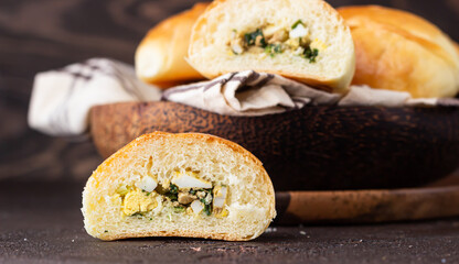 Traditional Russian pies with green onion and egg on wooden plate, dark rustic background. Russian...