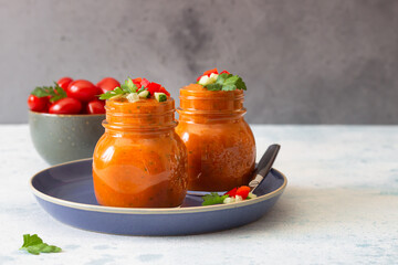 Traditional Spanish soup gazpacho with cucumber and tomato garnish. Summer homemade cold tomato cream soup in glass jars. Grey concrete background.