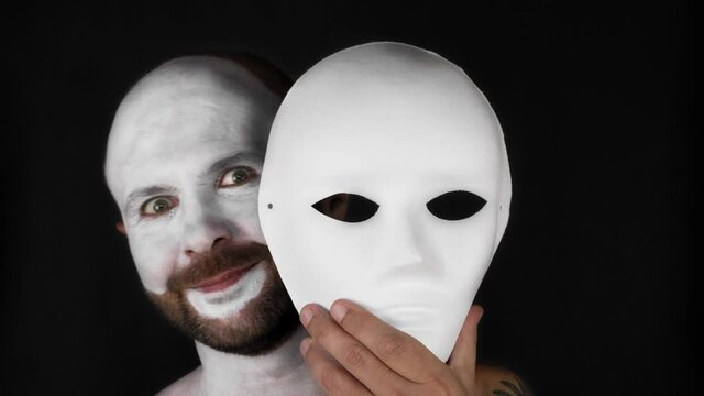 A mime man takes off a white theater mask. Man on a black background. 4k video.