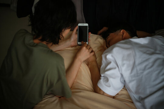 寝ている男性の指でスマートフォンの指紋認証を解除する女性
