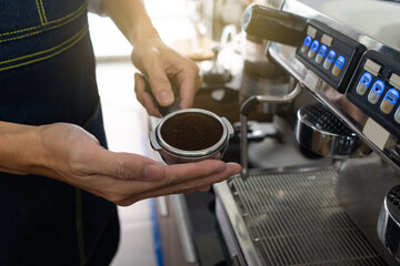 young asian man using coffee grinder machine to gride coffee beans in the cafe. barista concept