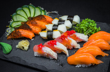 Sushi, traditional Japanese cuisine. Several delicious sushi on the decorated plate, black background. Group of sushi, Urakami, Nigori, Sushi jow, sashimi, tekamaki, etc ...