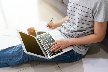 Naklejka premium A freelance asian woman using computer to work from home in the living room in the morning during covid-19 or coronavirus pandemic. new normal and technology concept