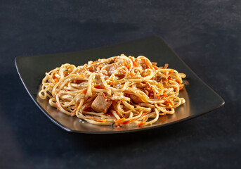 Dish of Japanese cuisine vermicelli on a black ceramic plate on a black background. Traditional dinner wheat vermicelli with chicken and paprika, prepared for removal to the hall. Oriental Restaurant.