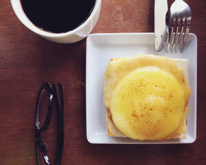 Delicious breakfast of cheesy egg and ham open face toasted sandwich, with local black coffee. Top view of table; flat lay arrangement