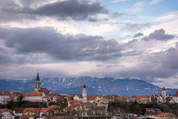 Panoramic view of medieval small town Kranj with Alps mountains covered with snow in the distance, Slovenia. Cloudy sky in winter season. Old churches with towers