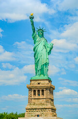 Fototapeta premium USA: The outdoor Statue of Liberty on a background of blue sky with white clouds on Liberty Island in New York, USA