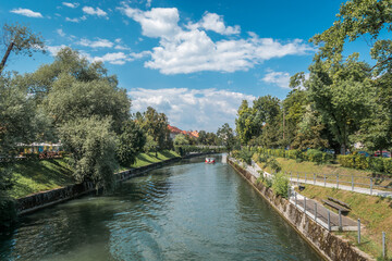 Fototapeta na wymiar Tourist boat in Ljubljanica river, Ljubljana, Slovenia. Beautiful sunny in amazing and very clean city. Sunny weather with some clouds in the sky. Elevated wide shot