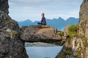 Young happy Asian woman sitting on Djevelporten or Devil's gate in Floya mountain hiking trail. A woman with smiley face. Svolvaer fishing village in Lofoten island, Scandinavia