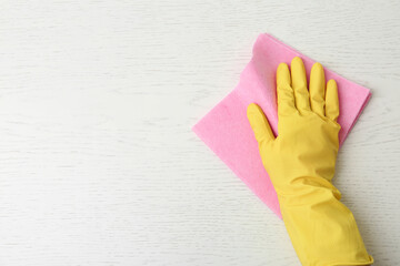 Person in gloves wiping white wooden table with rag, top view. Space for text