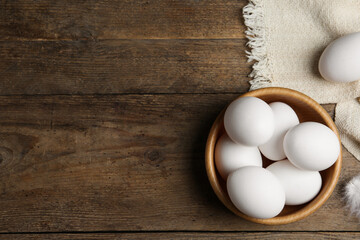 Many fresh raw chicken eggs in bowl on wooden table, flat lay. Space for text