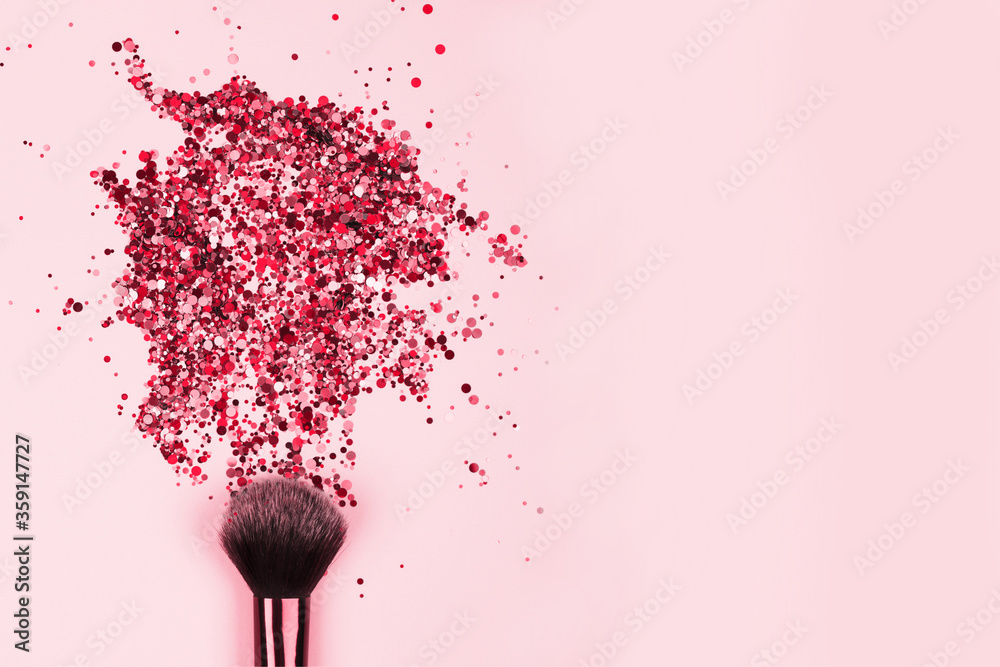 Poster closeup of professional cosmetics makeup brush with explosion of shiny pink colorful sparkles on bri