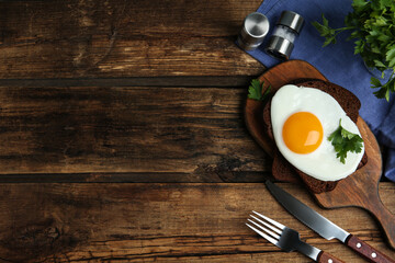 Tasty fried egg with parsley and rye bread on wooden table, flat lay. Space for text