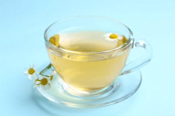 Delicious chamomile tea in glass cup on light blue background