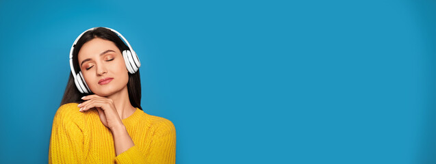 Young woman listening to music with headphones on blue background, space for text. Banner design