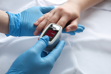 Doctor examining patient with modern fingertip pulse oximeter in bed, closeup