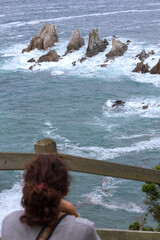 Gueirua beach, Asturias, Spain. Vertical view of tourist woman watching the rough sea breaking in the reef.