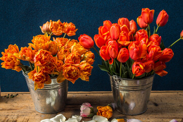 two bouquets of red and orange tulips in metal buckets on a wooden table on a dark background