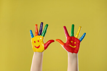 Kid with smiling faces drawn on palms against yellow background, closeup
