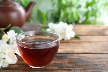 Cup of tea and fresh jasmine flowers on wooden table. Space for text