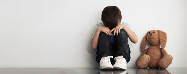 Sad little boy sitting near white wall, banner design with space for text. Time to visit child...