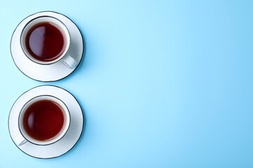 Cups of aromatic black tea on light blue background, flat lay. Space for text