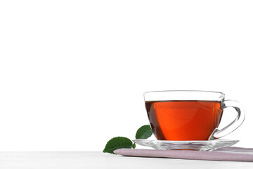 Glass cup of aromatic black tea and green leaves on table against white background. Space for text