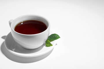 Cup of aromatic black tea and green leaves on white background