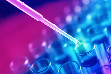 Dripping reagent into test tube with liquid sample on blurred background, closeup. Laboratory...