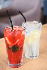 two summer refreshments with ice, lemon, strawberries, mint in tall glasses with a straw on a table in a restaurant. healthy lemonade. out of the house.