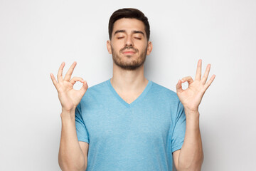 Concentrated relaxed man standing with closed eyes, having relaxation while meditating, trying to find balance and harmony isolated on gray. Yoga and meditation concept