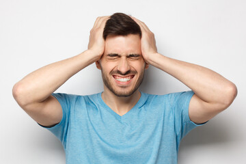 Naklejka premium Portrait of young man suffering from severe headache, holding head with both hands, closed eyes with helpless face expression, isolated on gray background