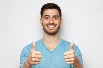Young happy man showing thumbs up, isolated on gray background